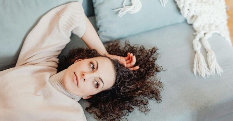 Donna riccia sdraiata sul divano con la mano appoggiata in maniera rilassata sulla testa