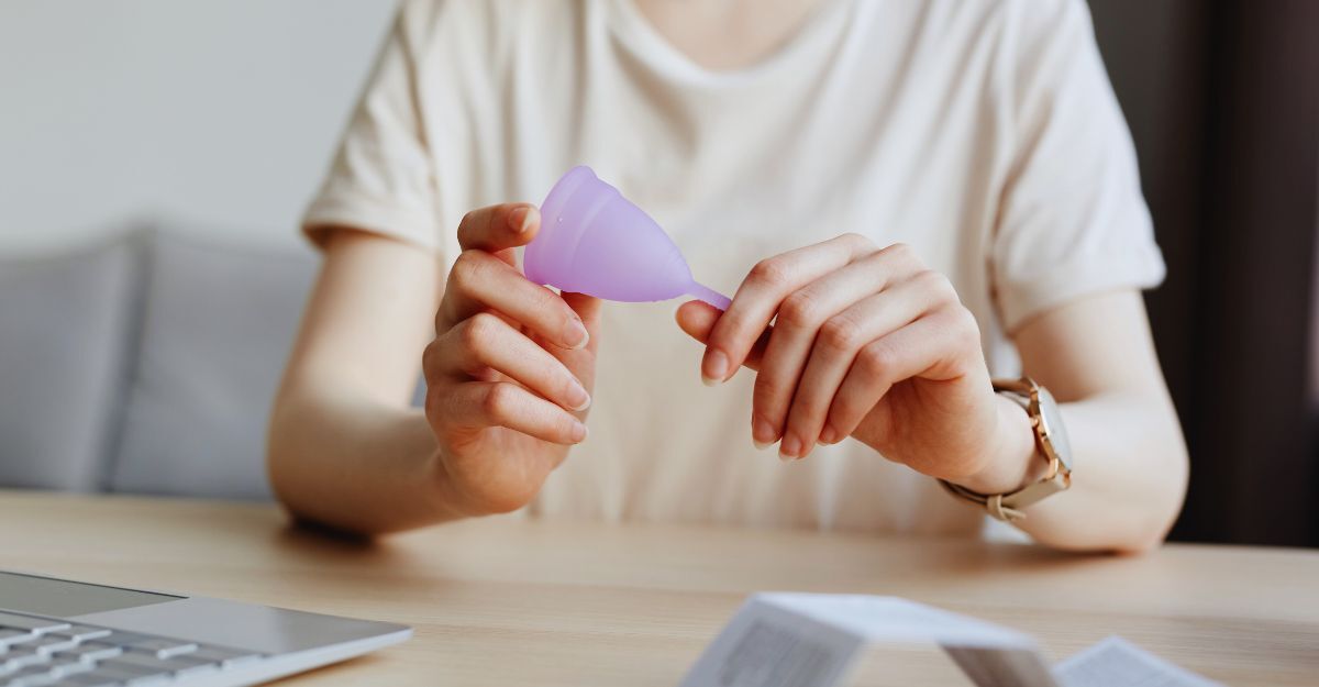 Donna che tiene fra le mani una coppetta mestruale di colore lilla mentre è seduta alla scrivania