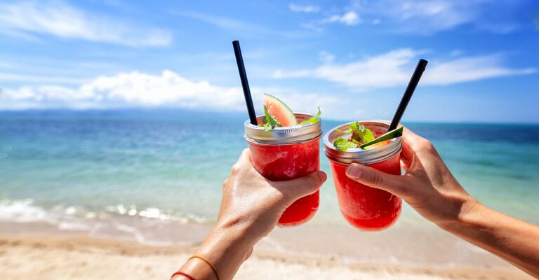 due persone brindano con un cocktail su una spiaggia tropicale