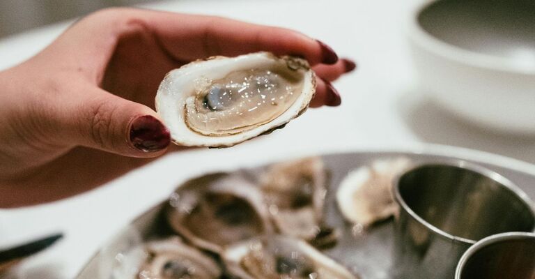 Una donna tiene in mano un'ostrica davanti a una tavola