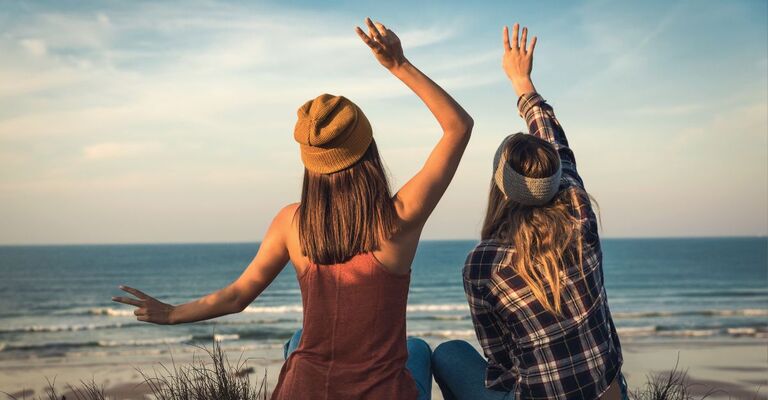ragazze di schiena alzano le braccia e guardano il mare
