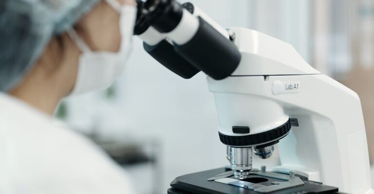 Ricercatrice osserva campione al microscopio in laboratorio