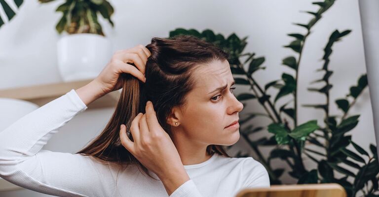 Donna che controlla il suo cuoio capelluto davanti a uno specchio sul tavolo