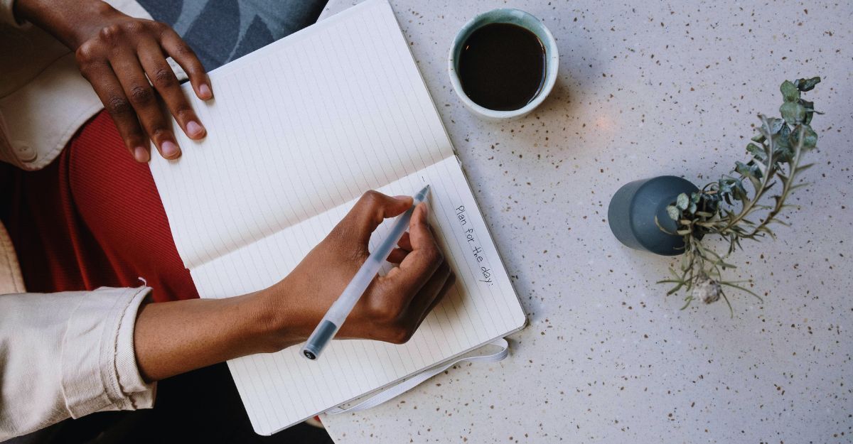 Primo piano di una donna che scrivere su un quaderno con la penna, con accanto una tazza di caffè