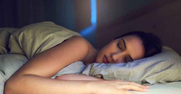Una donna dorme nel letto con luce soffusa.
