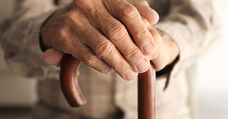 Una persona anziana appoggiata a un bastone.