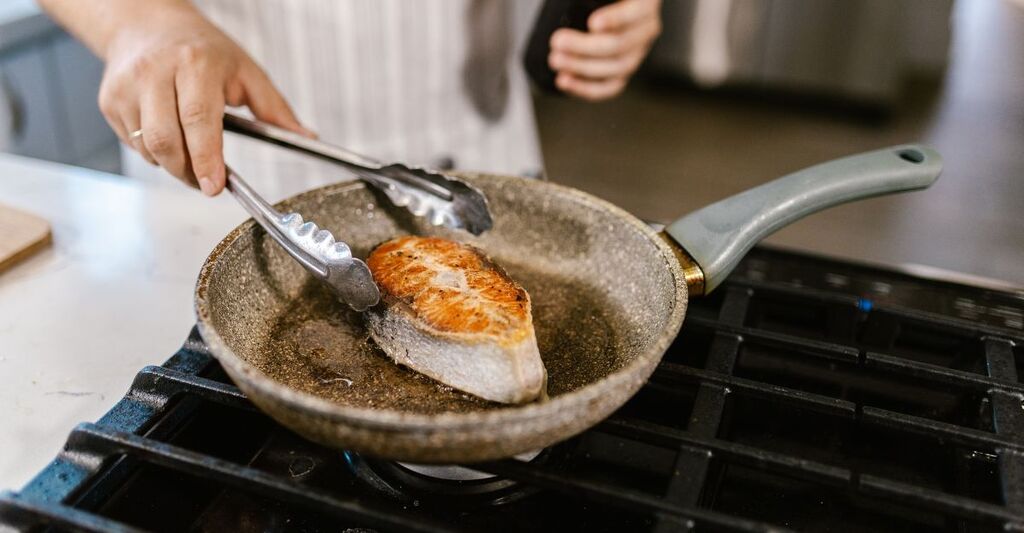Primo piano di persona che cucina un trancio di salmone in padella