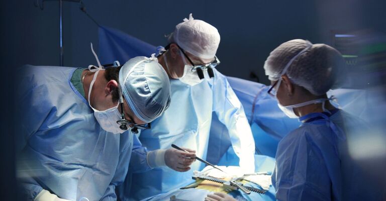 Equipe di chirurghi in sala operatoria durante un intervento, con indumenti sterili e strumenti chirurgici, in un ambiente ospedaliero sterile e tecnologico.