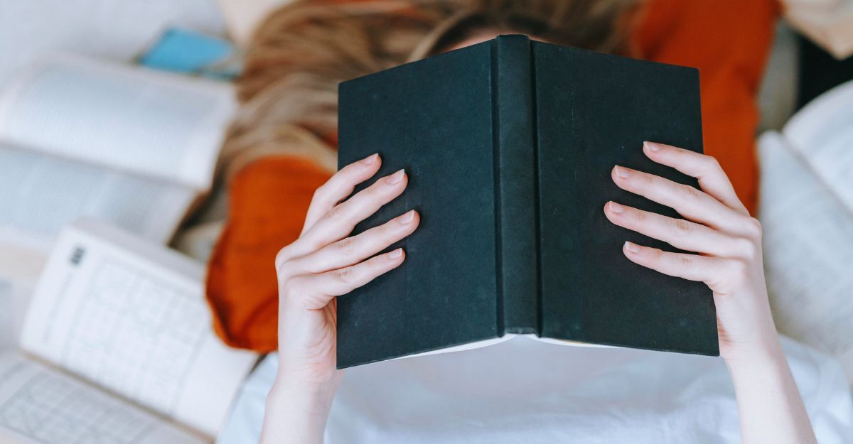 Ragazza sdraiata sul letto con un libro aperto davanti alla faccia