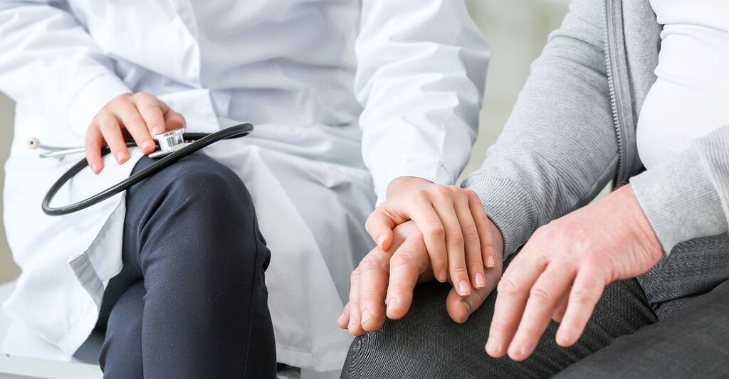 Medico che offre supporto a un paziente, tenendogli la mano durante una visita. Concetto di empatia, cura e assistenza sanitaria.