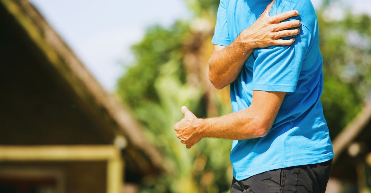 Uomo all'aperto con espressione dolorante mentre si tiene la spalla, sintomo comune di infiammazione alla cuffia dei rotatori.