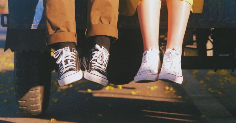 Primo piano di due paia di gambe che penzolano da una macchina. I due ragazzi indossano le scarpe Converse