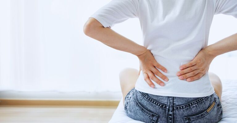 Donna di spalle con le mani all'altezza del coccige per un fastidio