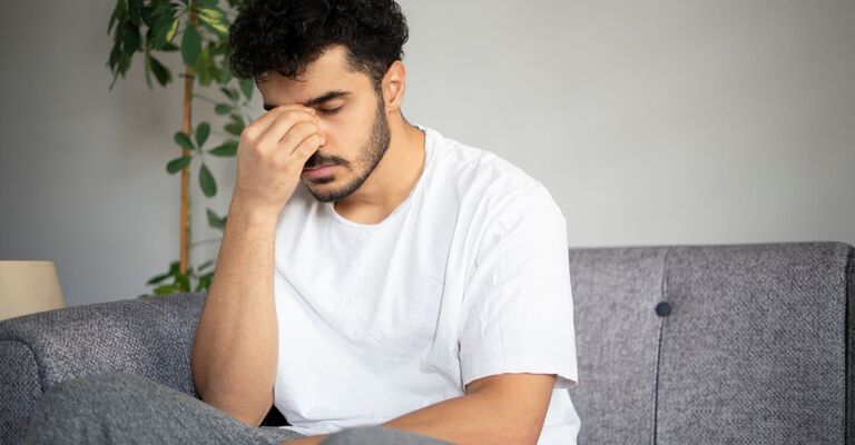 uomo seduto sul divano si tocca la fronte