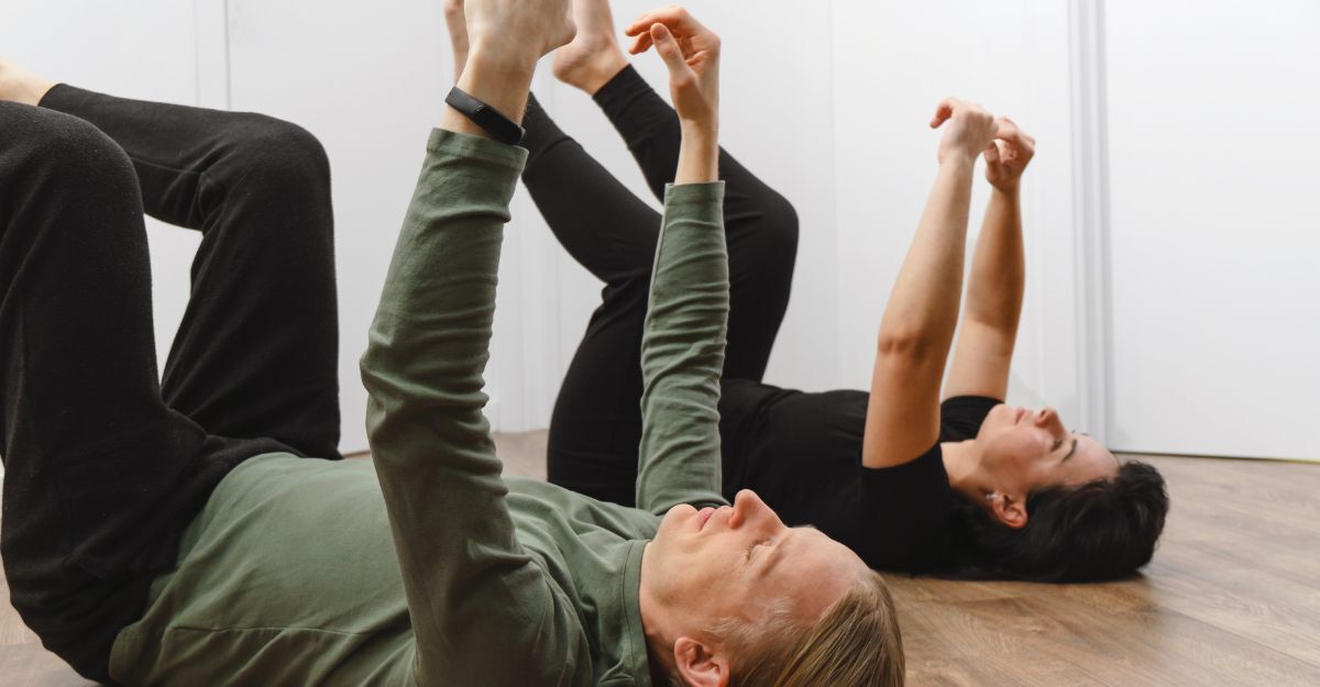 Due persone eseguono esercizi del metodo Feldenkrais sdraiate sul pavimento, con braccia e gambe sollevate.
