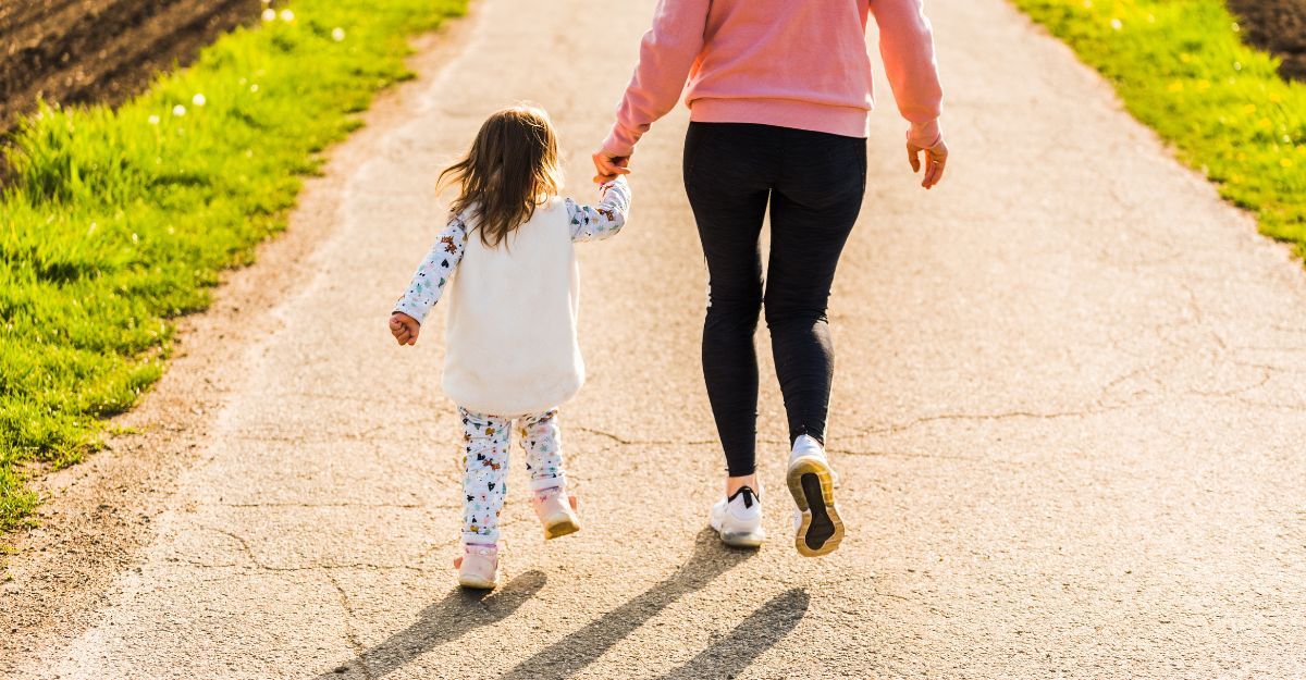 Mamma e bambina camminano mano nella mano su un sentiero di campagna in una giornata di sole.