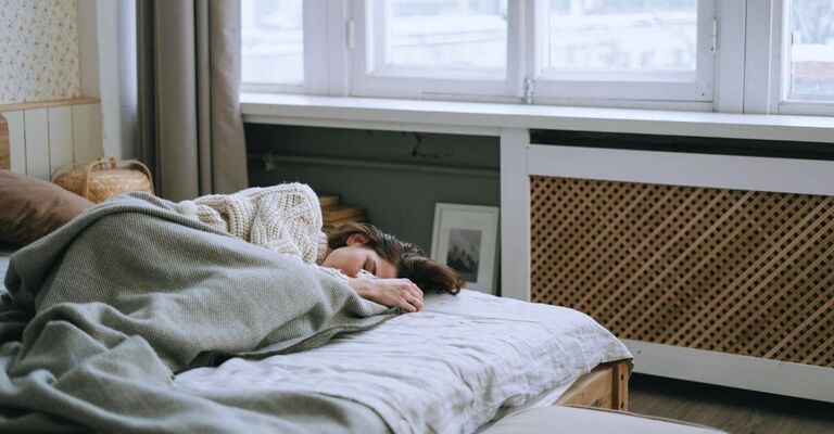 Ragazza sdraiata sul letto con una coperta addosso e gli occhi chiusi