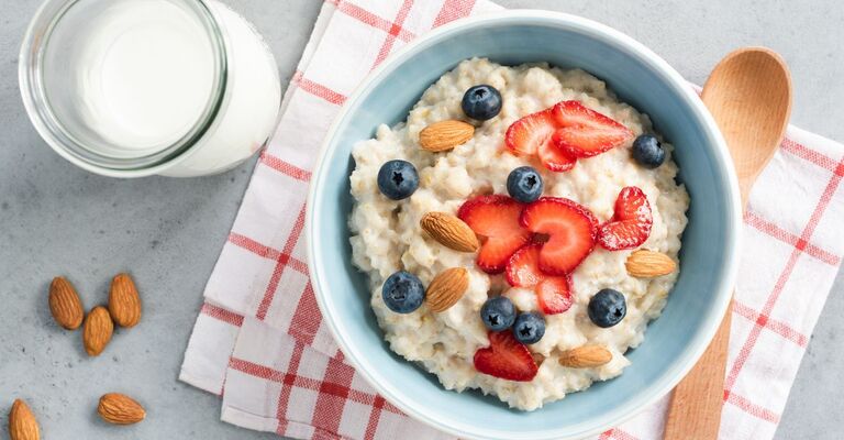 piatto con porridge mirtilli, fragole e mandorle, di fianco al piatto un bicchiere di latte