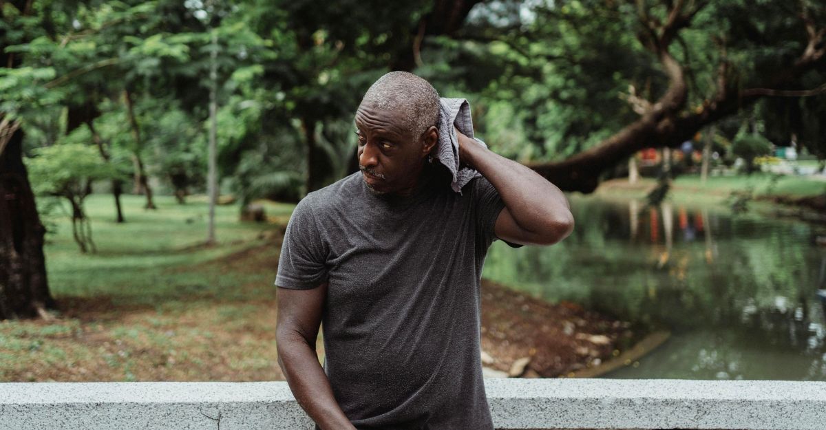 Un uomo in piedi per strada che si asciuga il retro della testa con un asciugamano grigio