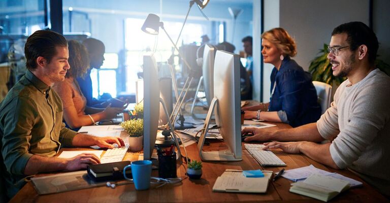 Primo piano di un gruppo di persone sorridenti che lavorano su computer in un ufficio moderno