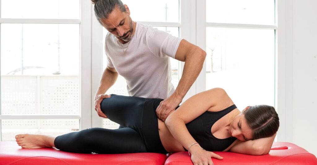 Fisioterapista che esegue una terapia manuale su una donna sdraiata sul fianco, lavorando sull'area dell'anca e del bacino per alleviare il dolore da psoas infiammato.
