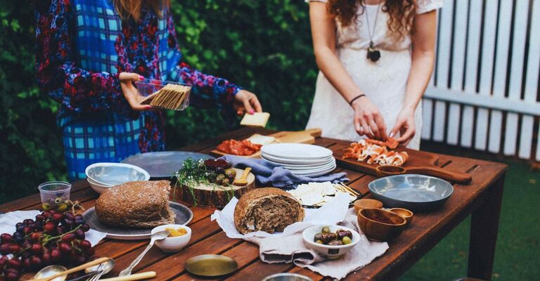 Menù di Ferragosto: ricette tradizionali e creative per pranzo o cena Primo piano su una tavolata con piatti e pietanze di vario tipo e due donne che stanno preparando alcune portate