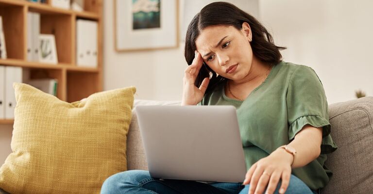 Donna che sul divano guarda il PC con occhi preoccupati