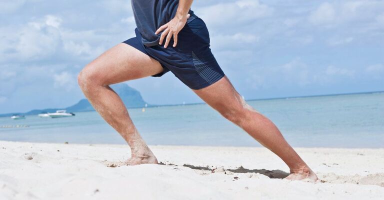 Un uomo pratica un esercizio di stretching del polpaccio in spiaggia.