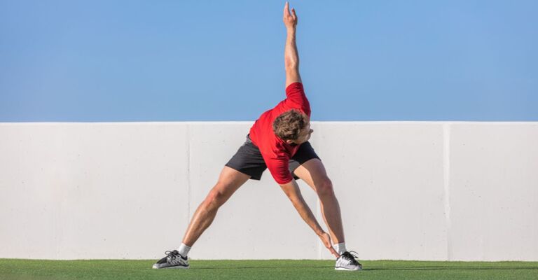Un uomo pratica stretching dinamico all'esterno.