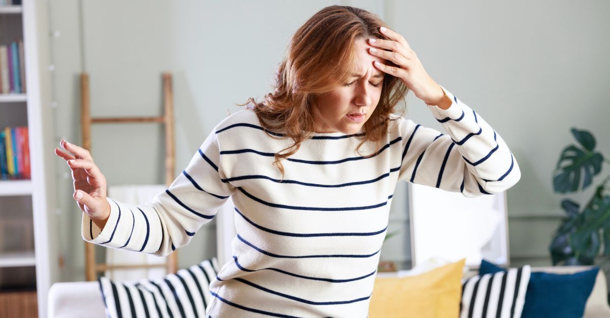 Giovane donna con maglia bianca a righe nere in piedi che si mette una mano sulla fronte con gli occhi chiusi mentre ha le vertigini
