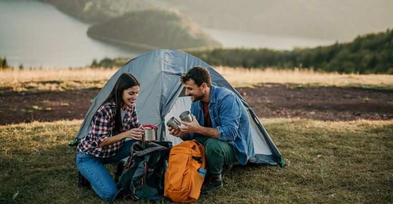 una coppia sorride seduta davanti ad una tenda da campeggio
