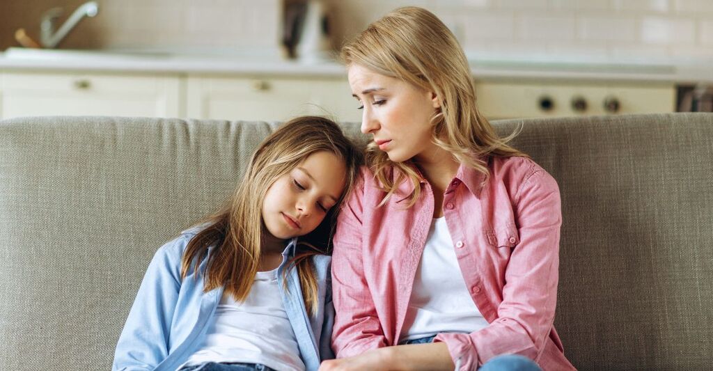 Mamma preoccupata è seduta sul divano con la figlia che poggia la testa a occhi chiusi sulla sua spalla