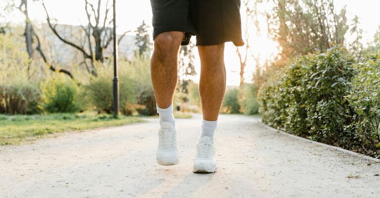 Primo piano di due gambe in pantaloncini e sneakers che camminano in un vialetto del parco