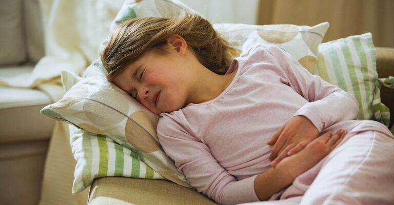 Bambina con dolori alla pancia sdraiata sul divano che soffre con gli occhi chiusi