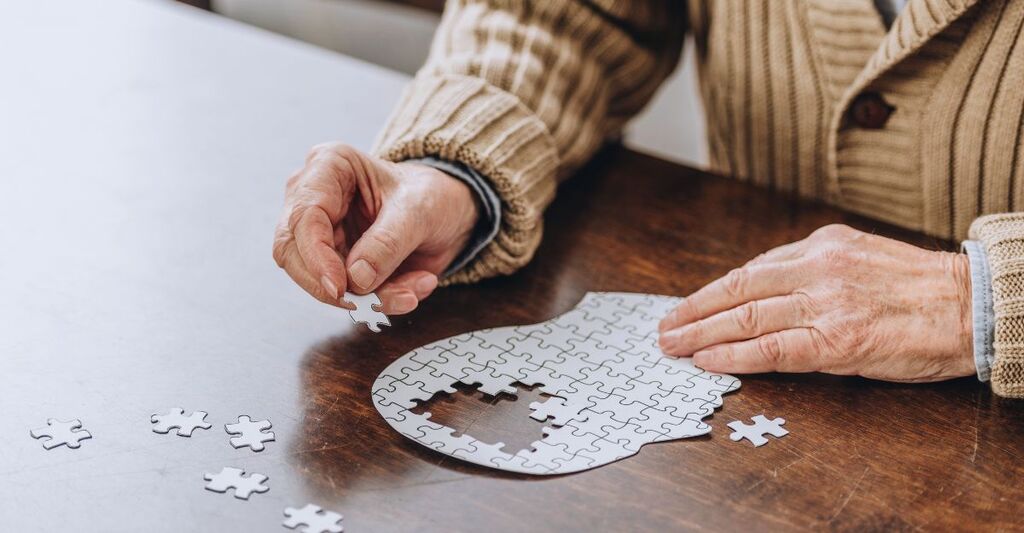Primo piano delle mani di una persona anziana che compongono un puzzle a forma di testa umana