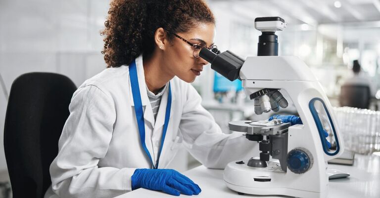 Giovane donna al microscopio durante una ricerca di laboratorio