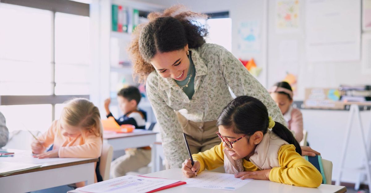 Maestra che sorride mentre osserva il lavoro di una sua alunna in classe