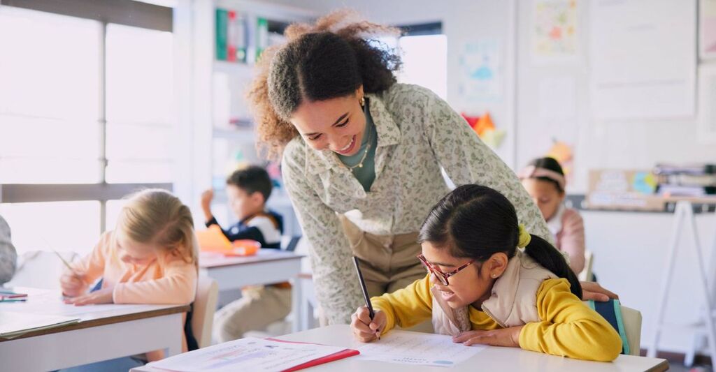 Maestra che sorride mentre osserva il lavoro di una sua alunna in classe