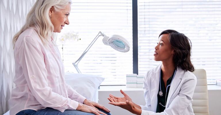 Primo piano di dermatologa che parla con una paziente anziana seduta sul lettino