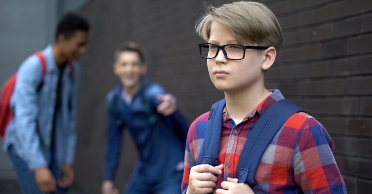 Bambino con zaino e occhiali vittima di prese in giro da coetanei, simbolo di bullismo e abusi verbali