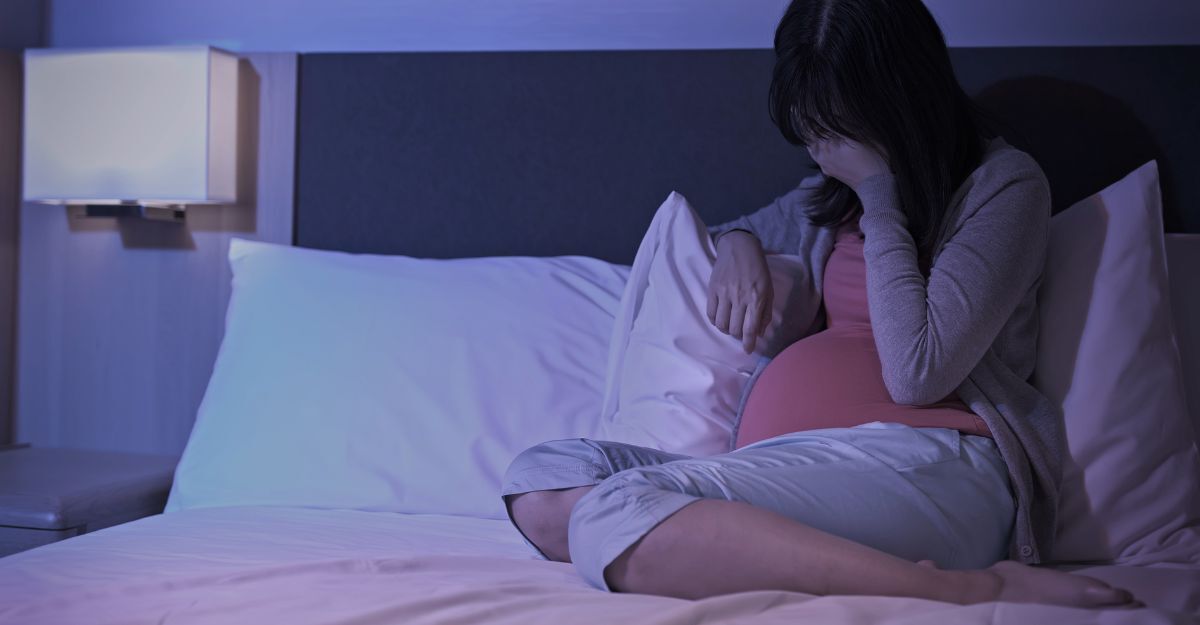Antidepressivi in gravidanza Donna incinta seduta sul letto di notte con una mano sul volto in segno di stanchezza o tristezza.