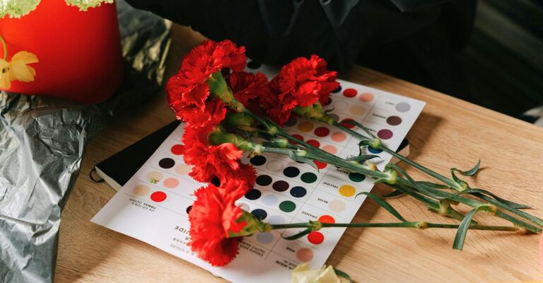 Garofani rossi recisi e appoggiati su una scala di colori appoggiata su un tavolo di legno chiaro