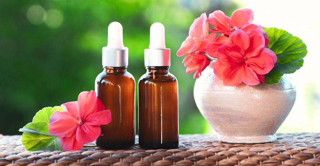 Bottigliette di olio essenziale di geranio rosa accanto a un vaso con fiori di geranio, utilizzato per aromaterapia, cura della pelle e rimedi naturali.