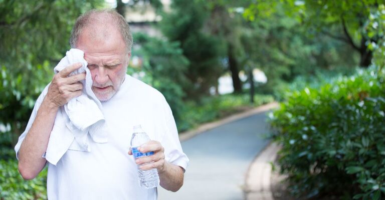 Un uomo anziano accaldato tiene una bottiglietta di acqua in mano.