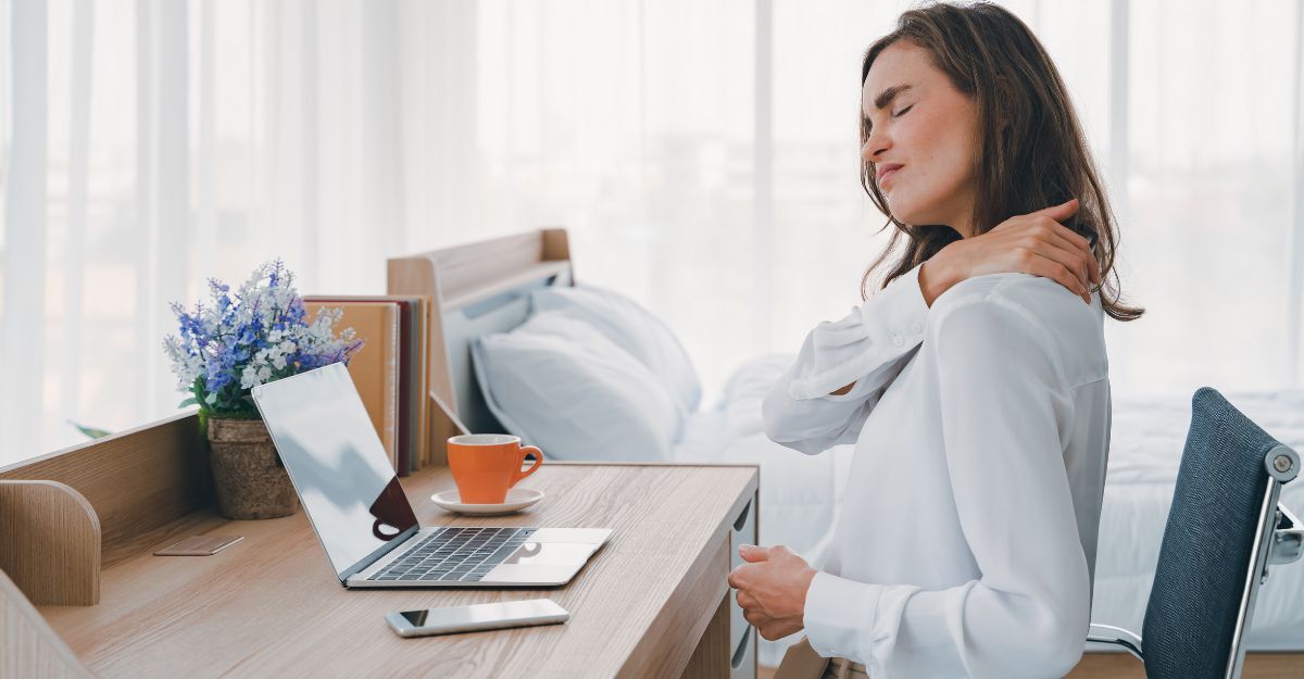 donna seduta alla scrivania, si tocca le spalle doloranti