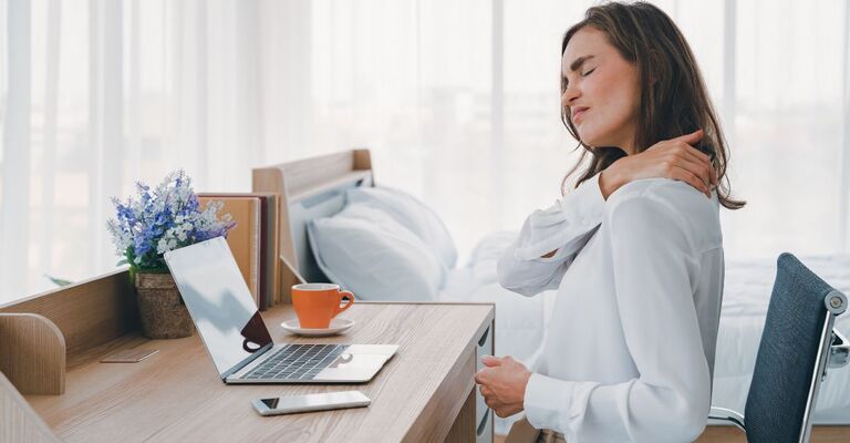 donna seduta alla scrivania, si tocca le spalle doloranti