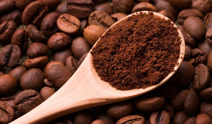 Un mestolo di caffè macinato con chicchi di caffè sullo sfondo.