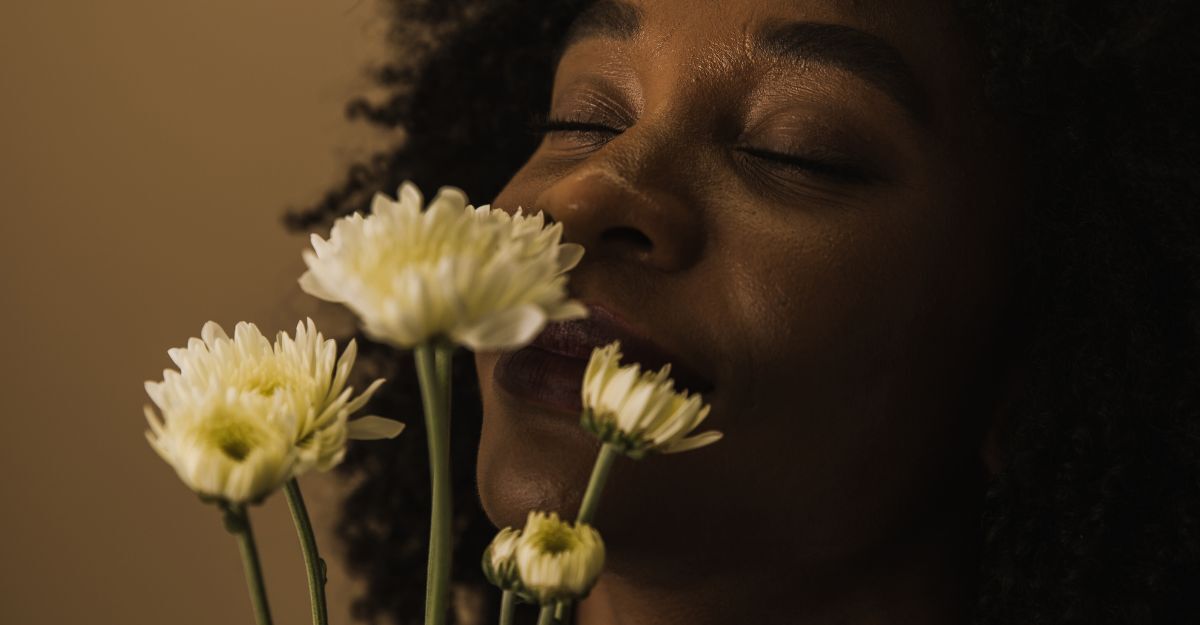 Primo piano di una donna che chiude gli occhi e annusa dei fiori bianchi.