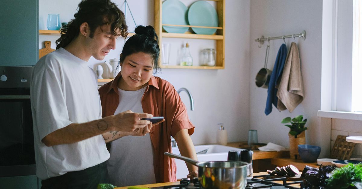 Due ragazzi in cucina con una pentola sul fuoco che controllano insieme la ricetta sul cellulare