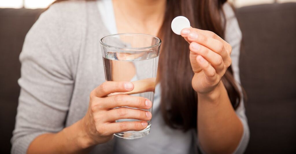 donna tiene con una mano un bicchiere d'acqua e con l'altra una pastiglia